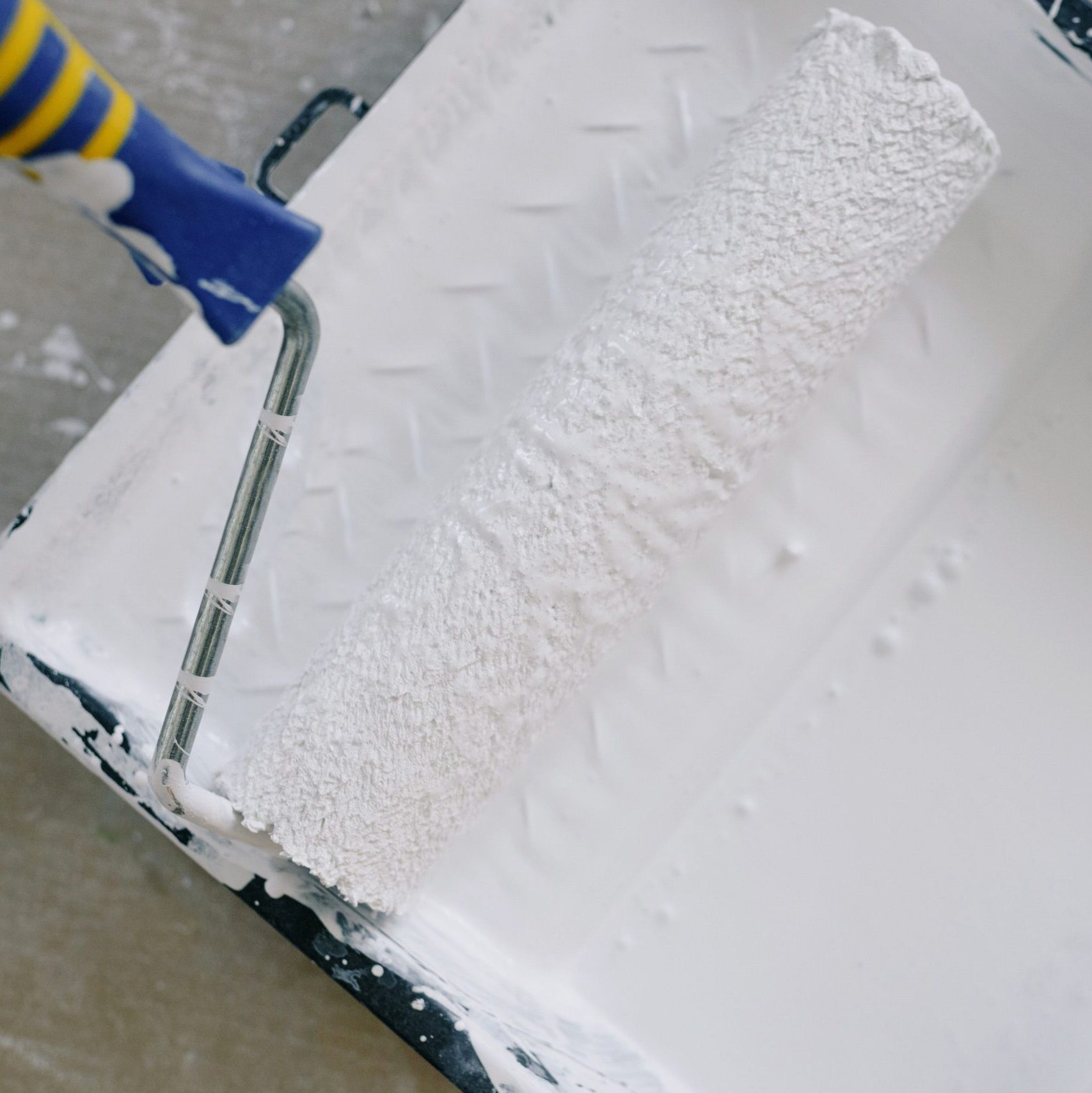 Top view paint roller placed in black tray filled with white pigment and placed on floor in renovating apartment